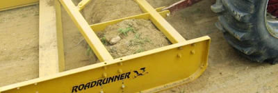 Yellow Roadrunner agricultural equipment with black text branding on sandy ground