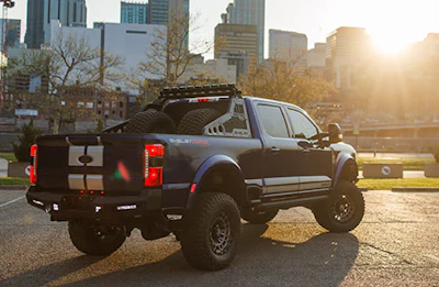 Lifted black pickup truck with custom rear cargo bed parked in urban setting at sunset with city skyline