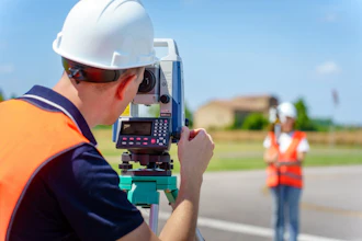 Surveyor in safety gear using theodolite to measure land with assistant in background