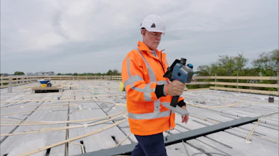 Construction worker in orange safety vest and white hard hat holding surveying equipment on rooftop