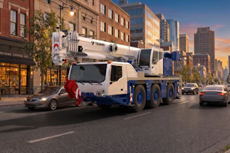 White and blue Tadano mobile crane truck on urban city street at sunset with buildings and traffic