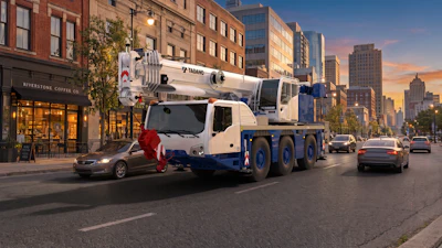 White and blue Tadano mobile crane truck on urban city street at sunset with buildings and traffic