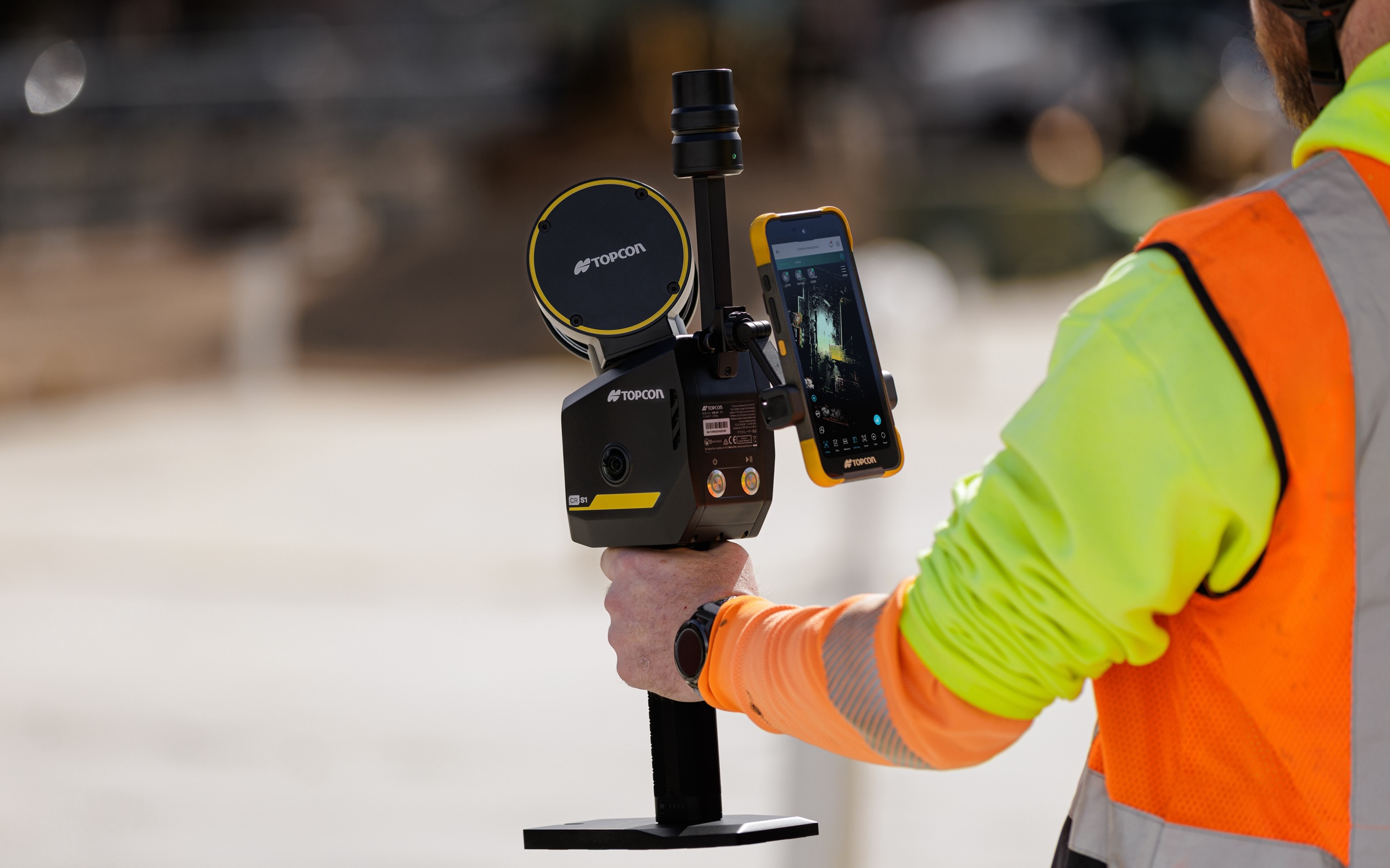 Construction worker in safety gear holding surveying equipment with smartphone display on job site