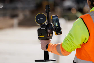 Construction worker in safety gear holding surveying equipment with smartphone display on job site