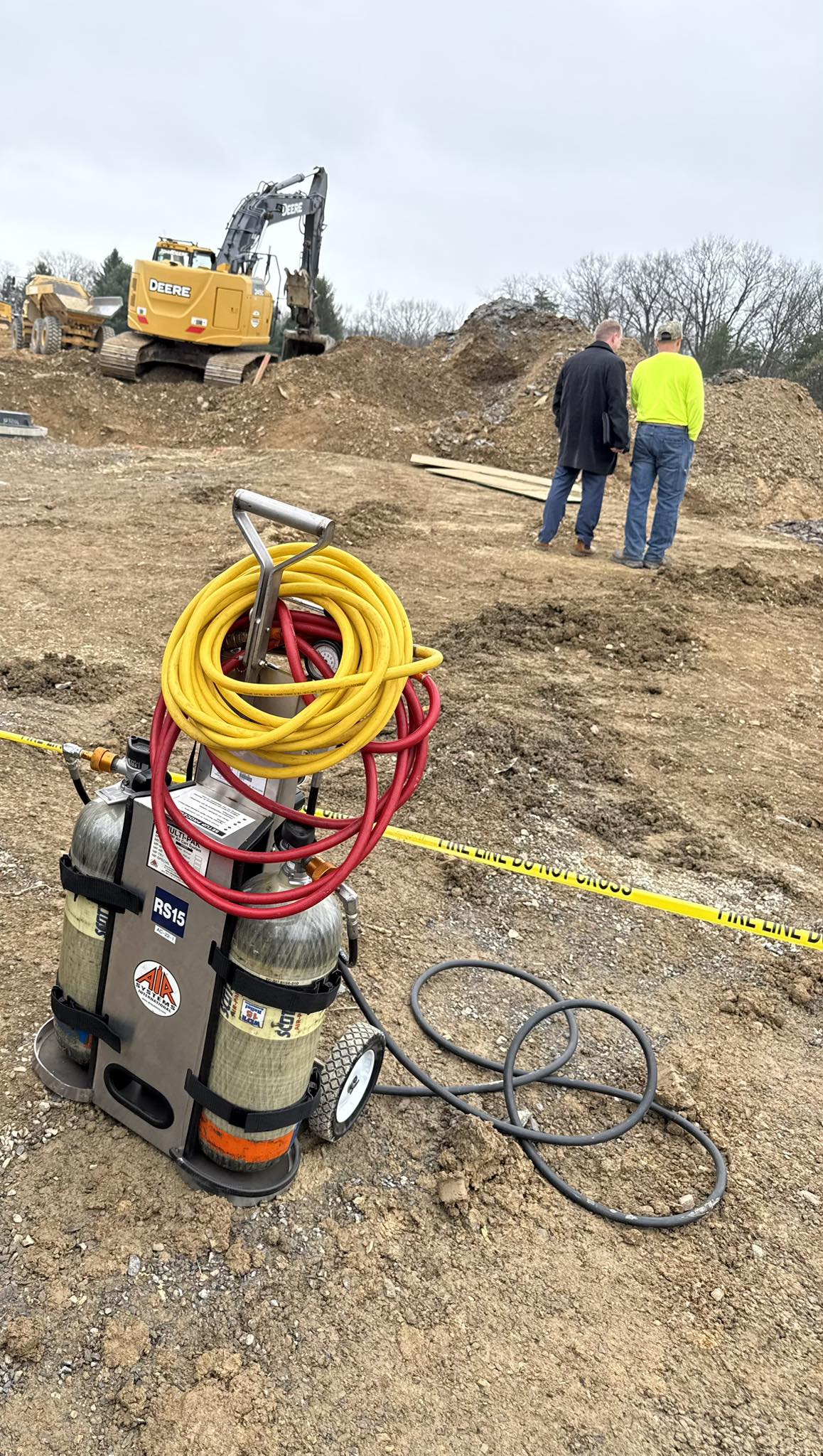Franklin County, Pennsylvania site of fatal trench collapse with yellow excavator, workers in safety gear, and equipment including hoses on dirt ground