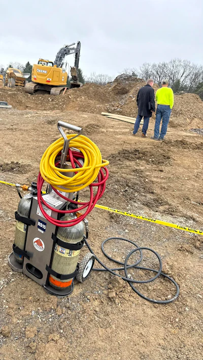 Franklin County, Pennsylvania site of fatal trench collapse with yellow excavator, workers in safety gear, and equipment including hoses on dirt ground