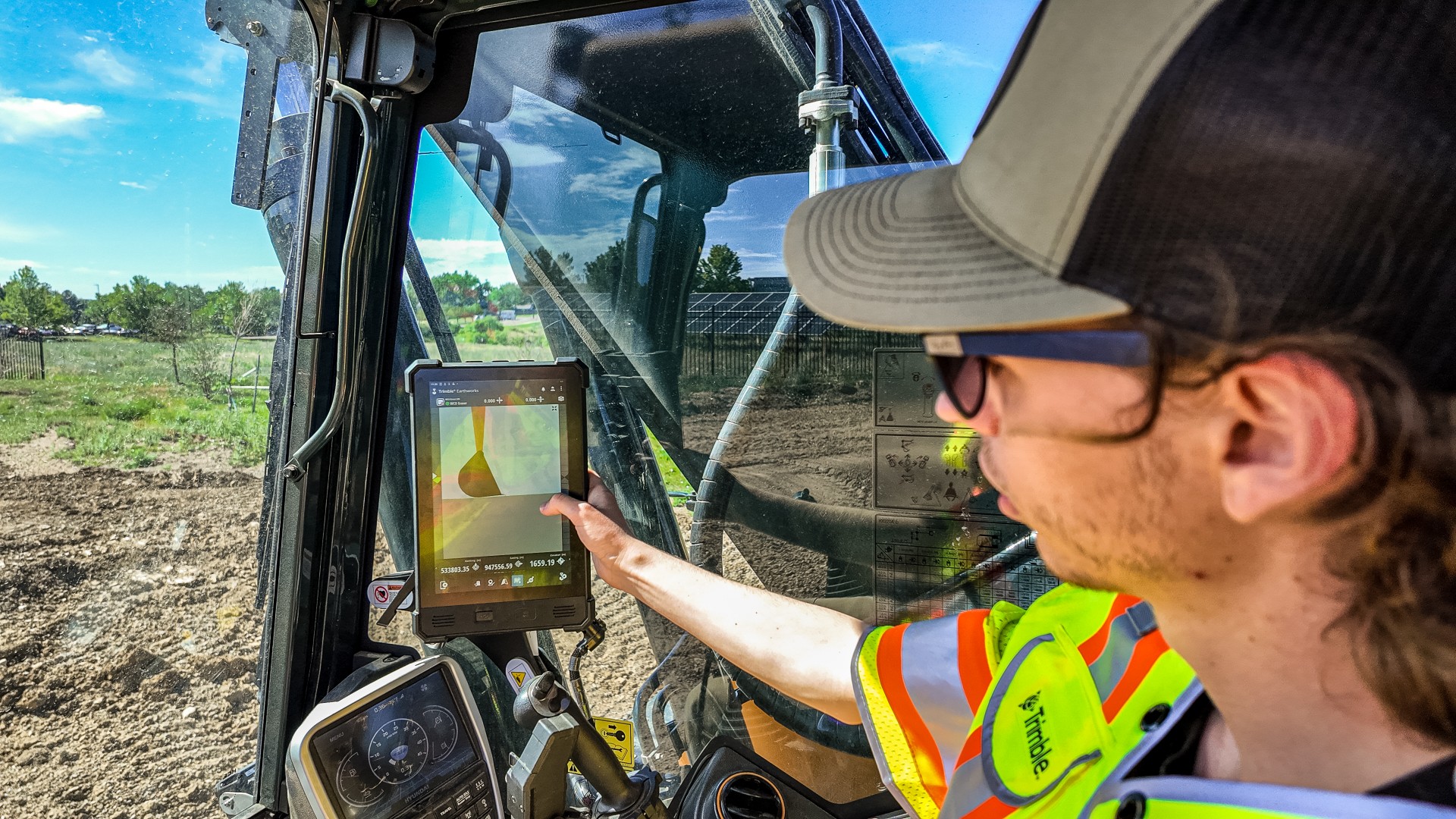 Construction worker in safety gear operating excavator while viewing surveying data on tablet in outdoor work site
