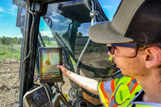 Construction worker in safety gear operating excavator while viewing surveying data on tablet in outdoor work site