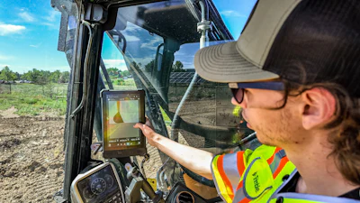 Construction worker in safety gear operating excavator while viewing surveying data on tablet in outdoor work site
