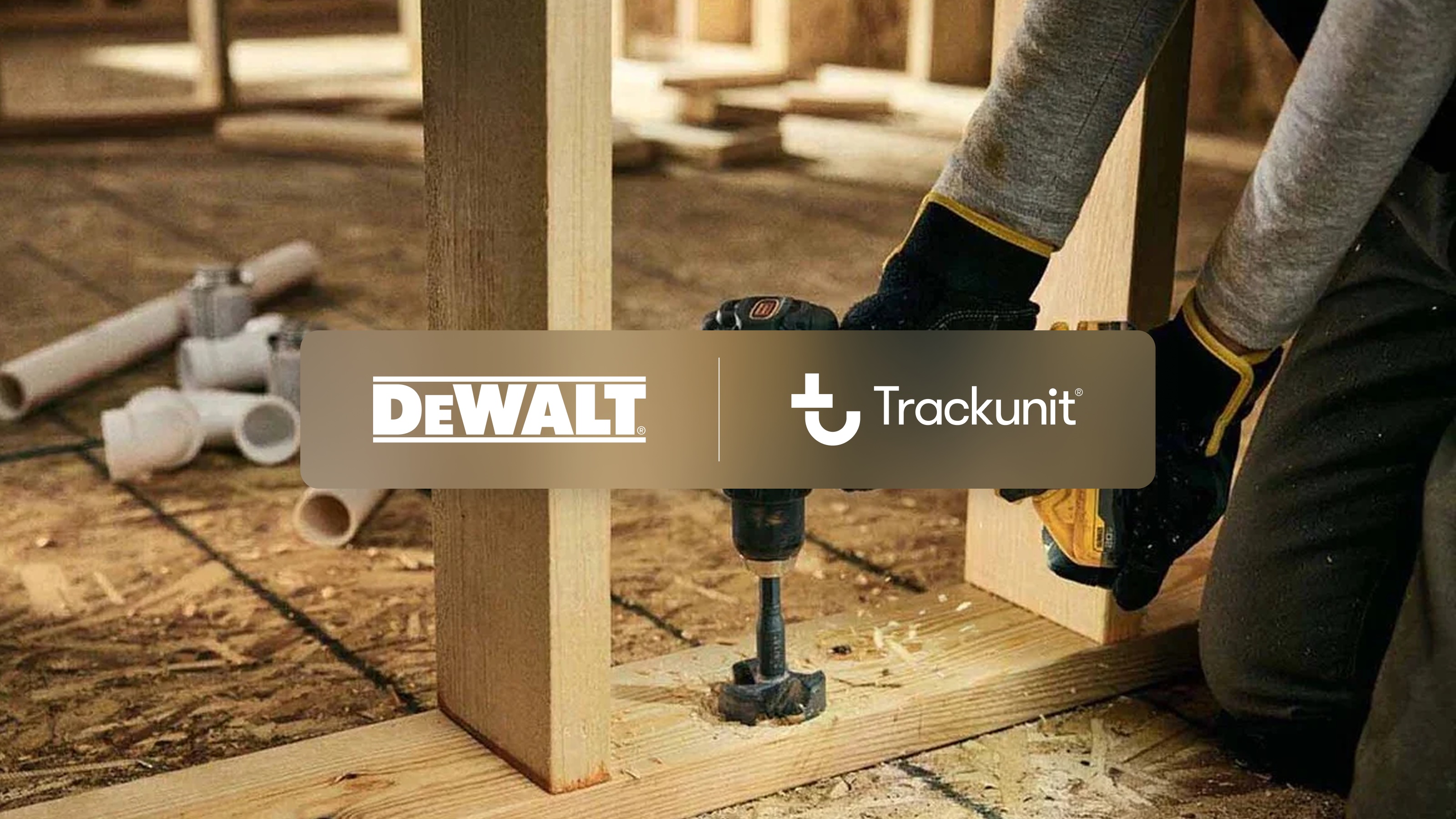 Worker using DEWALT drill on wooden frame in construction workshop with Trackunit branding