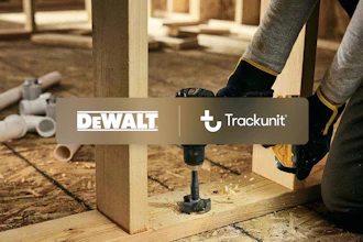 Worker using DEWALT drill on wooden frame in construction workshop with Trackunit branding