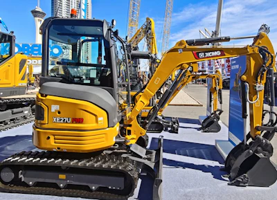 Yellow XCMG 2.7-metric-ton XE27U Pro mini excavator on display at construction equipment trade show ConExpo 2026 with cranes and buildings in background